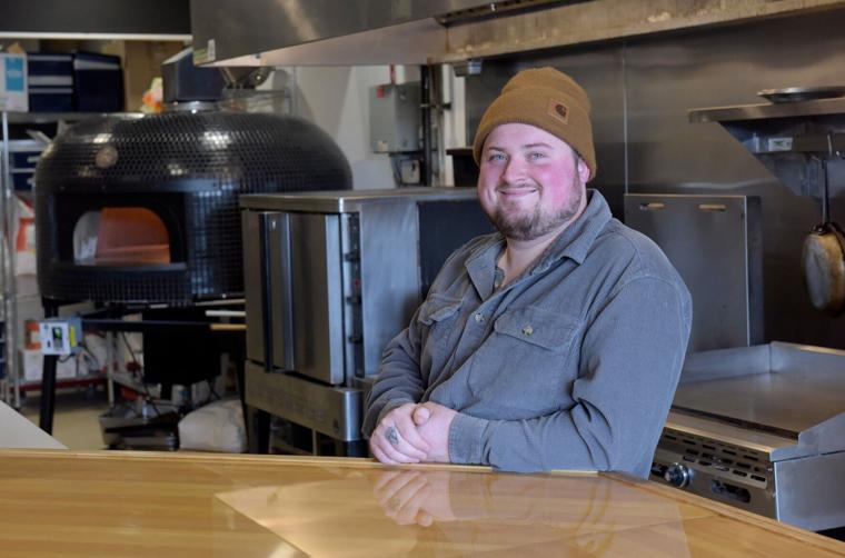 Josh Buxton at the counter of his restaurant, the oven glowing behind him